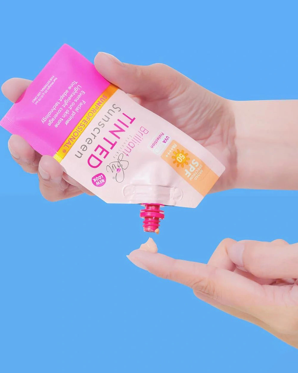 Hand dispensing Brilliant Skin Tinted Sunscreen from a pink spout pouch onto a fingertip against a blue background