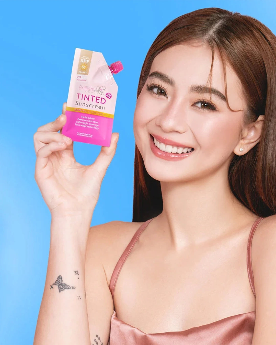 Smiling model holding Brilliant Skin Tinted Sunscreen SPF 50 pink pouch beside her face