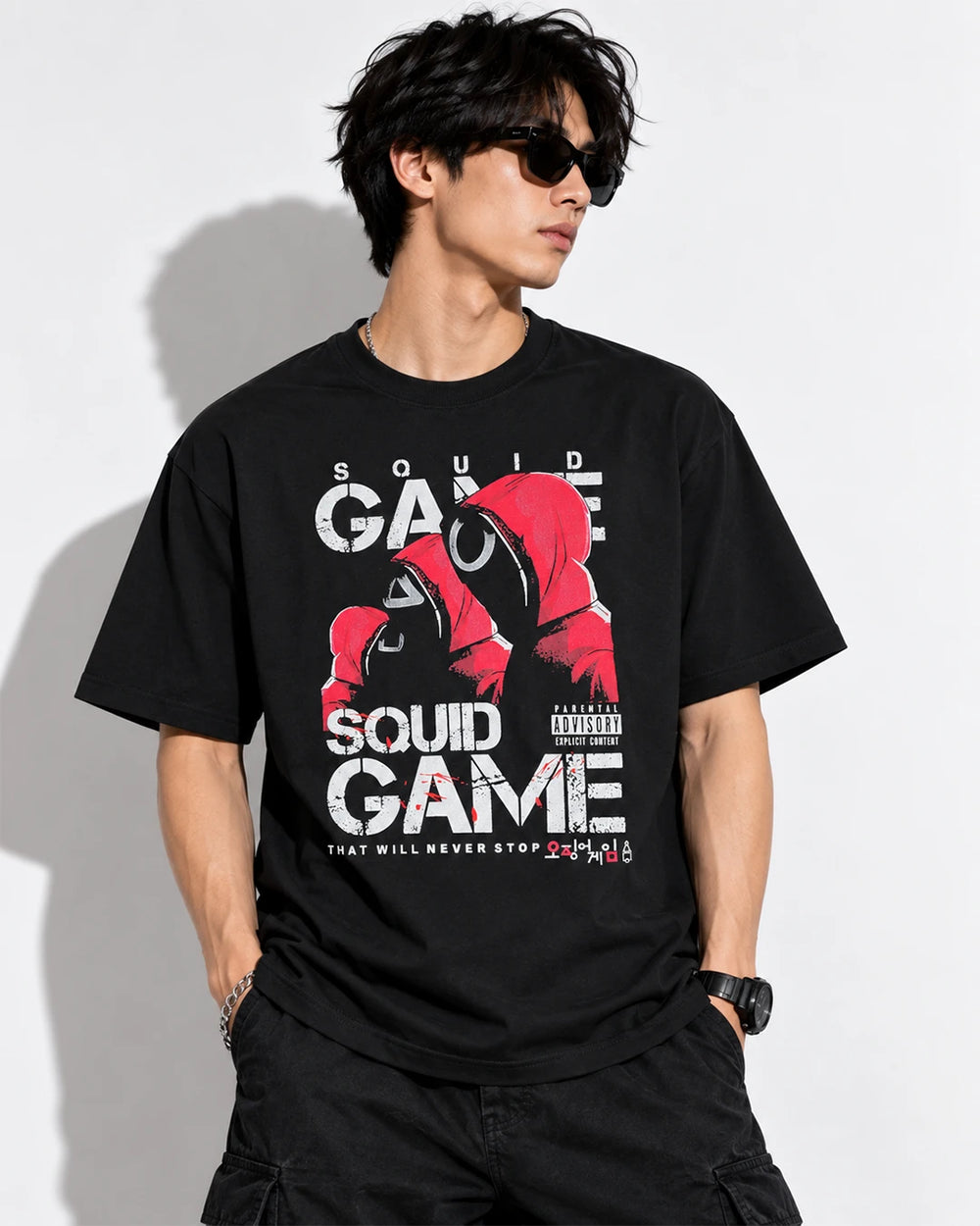 Model wearing black Squid Game graphic T-shirt with red guards and circle-mask design, front view